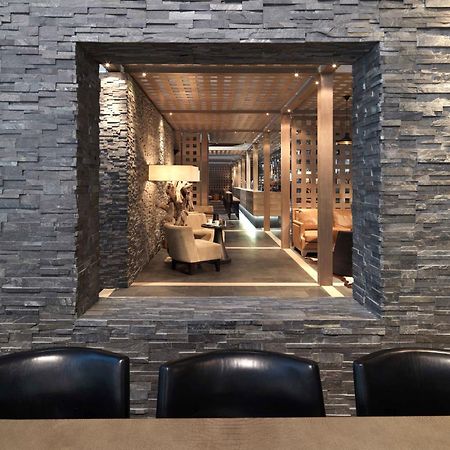 Dubai International Terminal Hotel Exterior foto The photo shows a stylish interior space, framed by a wall made of stacked stone. Within the frame, there is a cozy seating area featuring beige chairs and a wooden table. Soft lighting highlights the modern decor, which includes wooden beams and par