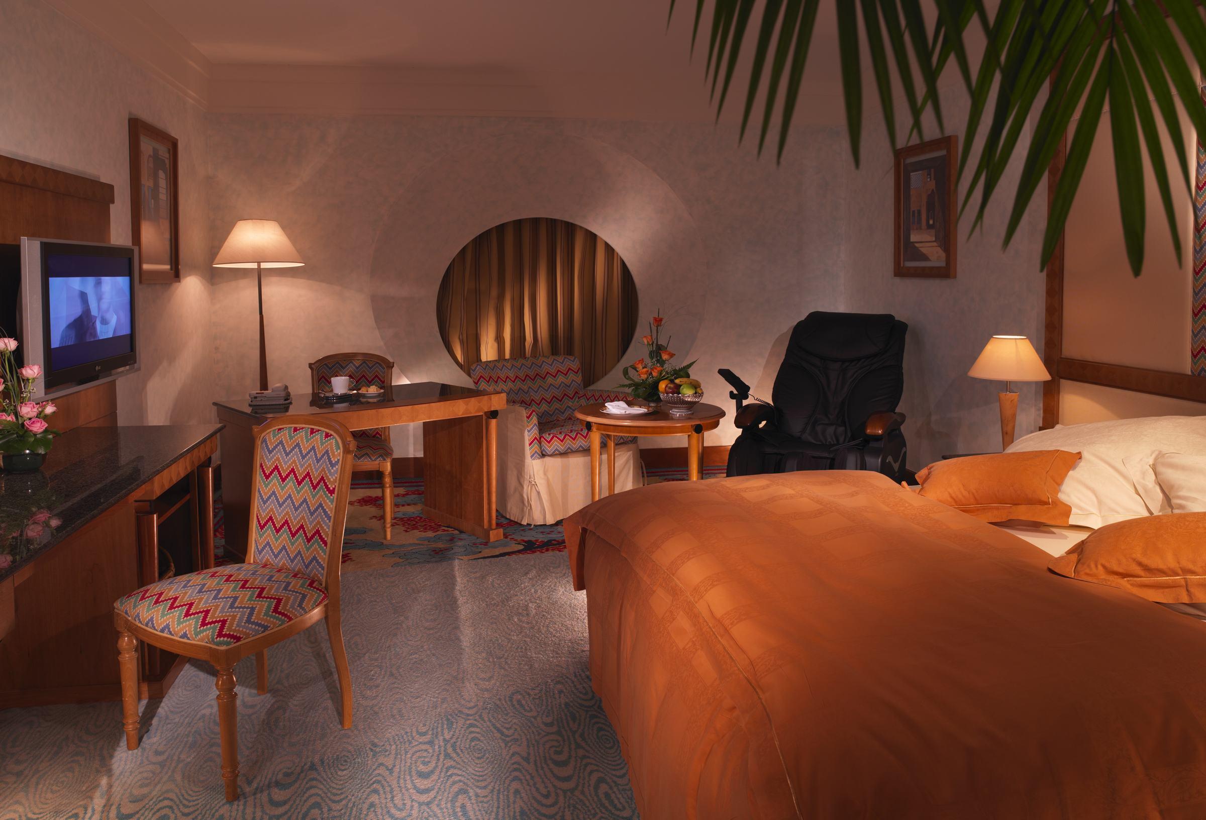 Dubai International Terminal Hotel Exterior foto The photo shows an interior view of a hotel room. The room features a large bed with orange bedding and a decorative headboard. There is a chair with a colorful, patterned upholstery next to a wooden desk, which also has a small arrangement of flower