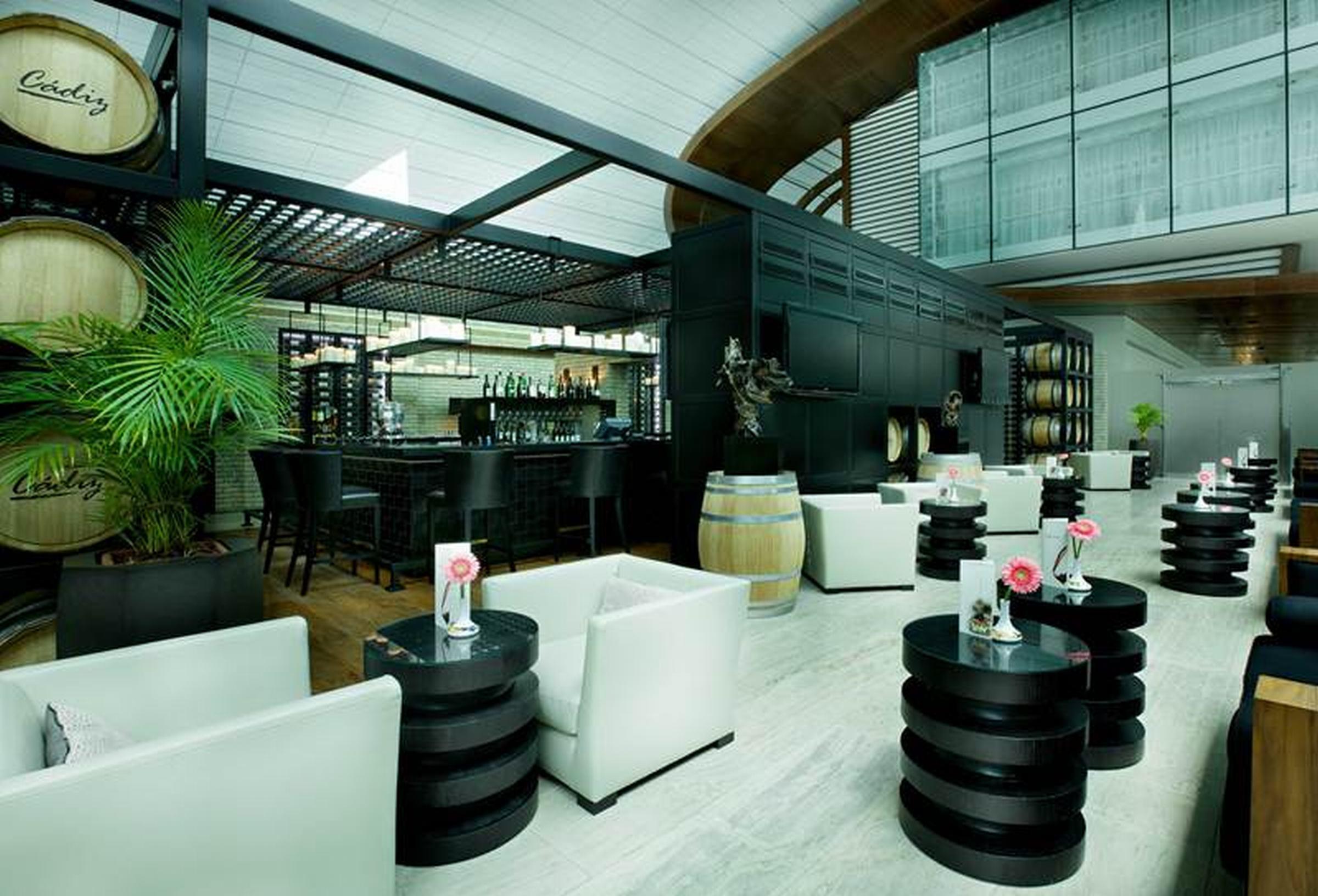Dubai International Terminal Hotel Exterior foto The photo depicts a modern restaurant interior. It features a sleek bar area with black cabinetry and a stylish, minimalist design. The seating arrangement includes white chairs paired with round black tables. In the background, there are decorative 