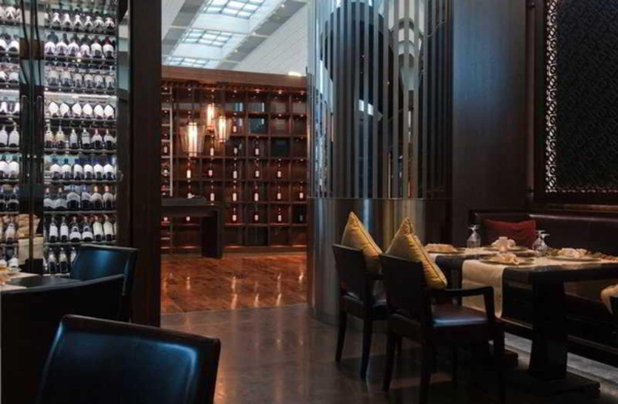 Dubai International Terminal Hotel Restaurante foto The photo shows an elegant restaurant interior. The design features dark wood elements, creating a sophisticated atmosphere. On one side, there is a wall lined with wine bottles, while the opposite wall has shelves that appear to hold more decorative