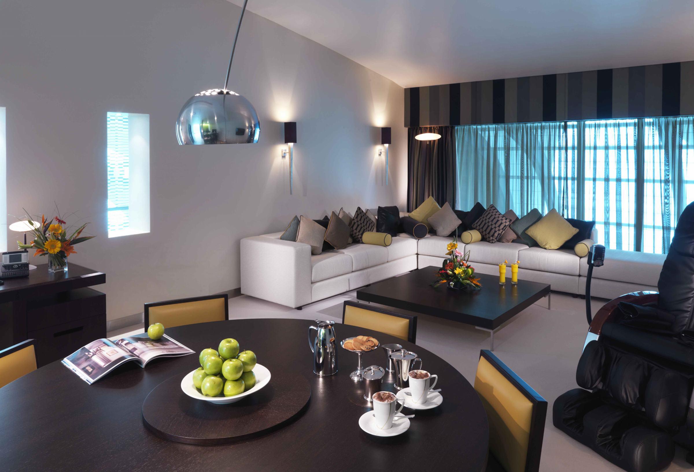 Dubai International Terminal Hotel Quarto foto The photo shows a modern living room with a stylish design. There is a large, white sectional sofa adorned with various colorful cushions. A dark coffee table sits in the center, featuring a bowl of green apples, a few elegant cups, and a magazine. B