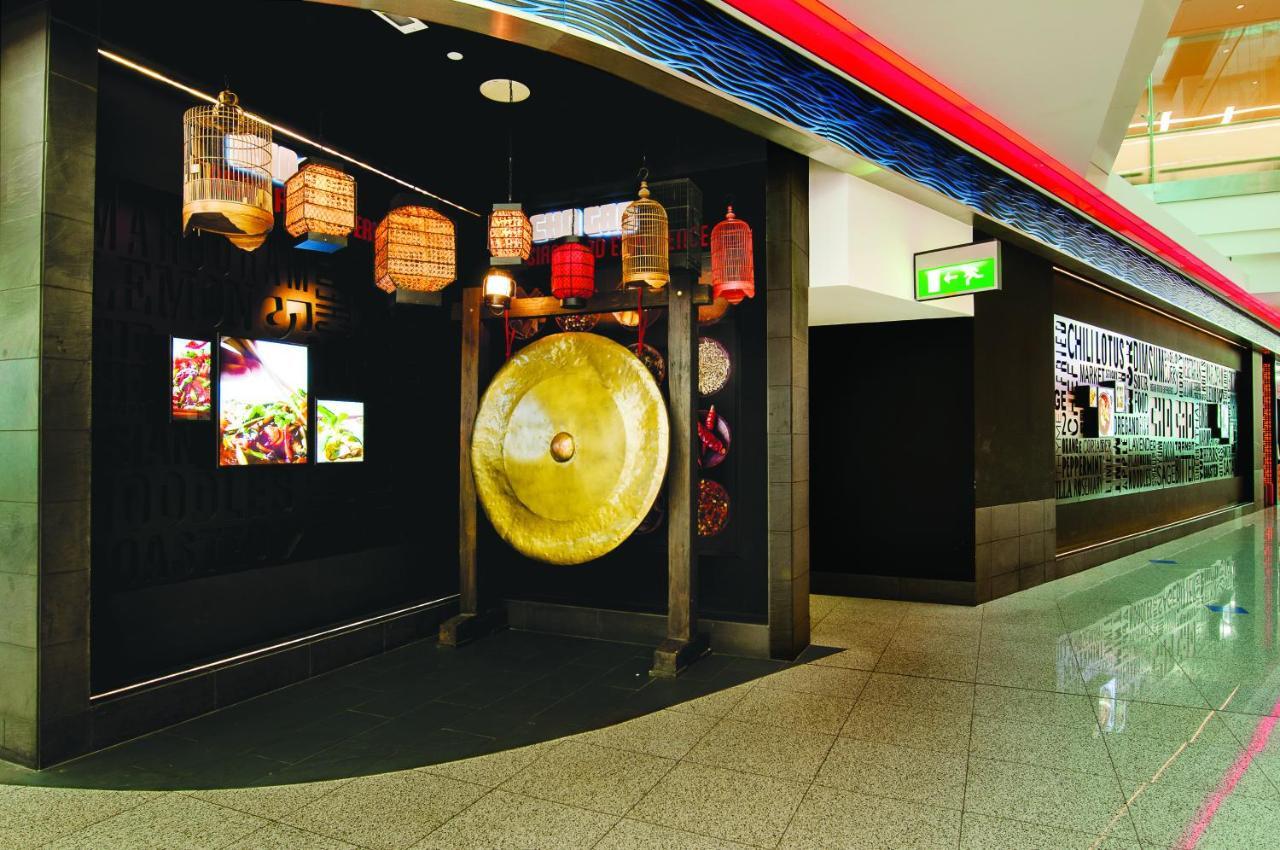 Dubai International Terminal Hotel Exterior foto The photo shows an entrance to a restaurant or dining area decorated with Asian-inspired elements. There are colorful lanterns hanging from the ceiling, adding a warm ambiance. A large gong is prominently displayed on a stand, suggesting a theme rela