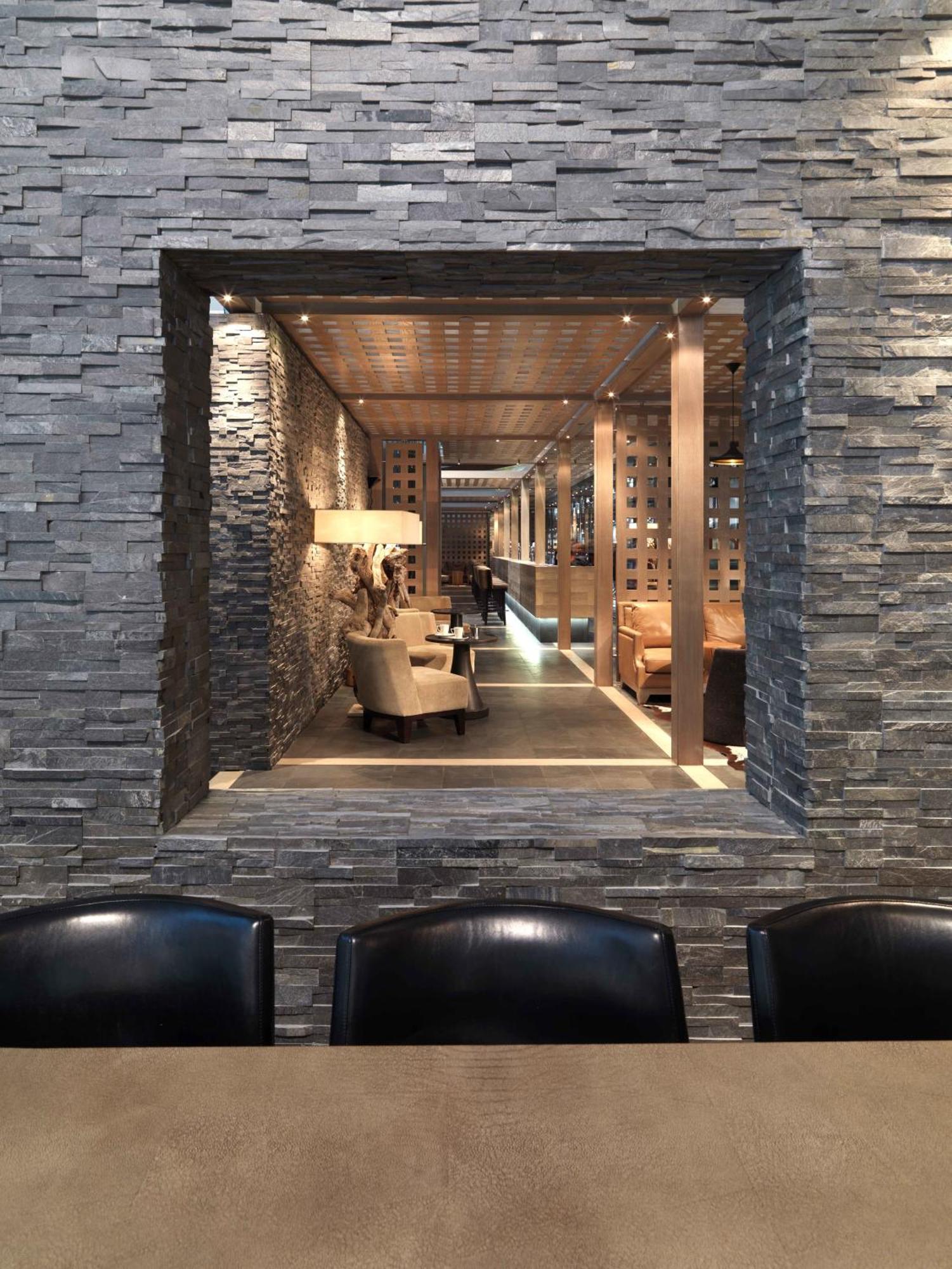 Dubai International Terminal Hotel Exterior foto The photo shows a stylish interior space, framed by a wall made of stacked stone. Within the frame, there is a cozy seating area featuring beige chairs and a wooden table. Soft lighting highlights the modern decor, which includes wooden beams and par