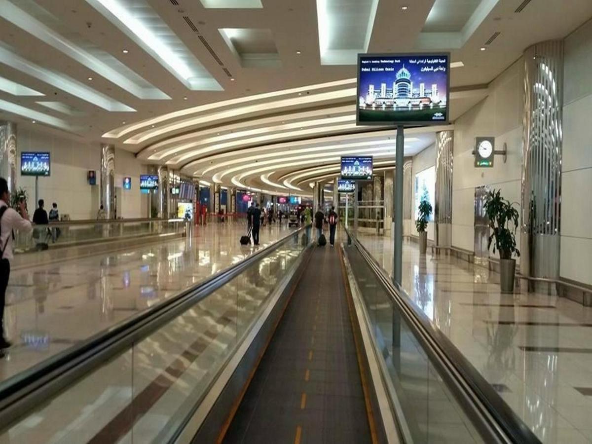 Dubai International Terminal Hotel Exterior foto The photo shows an airport interior with a modern and spacious design. There is a long moving walkway in the center, flanked by various shops and terminals. The ceiling features elegant lighting and a smooth, curved structure, creating a welcoming at