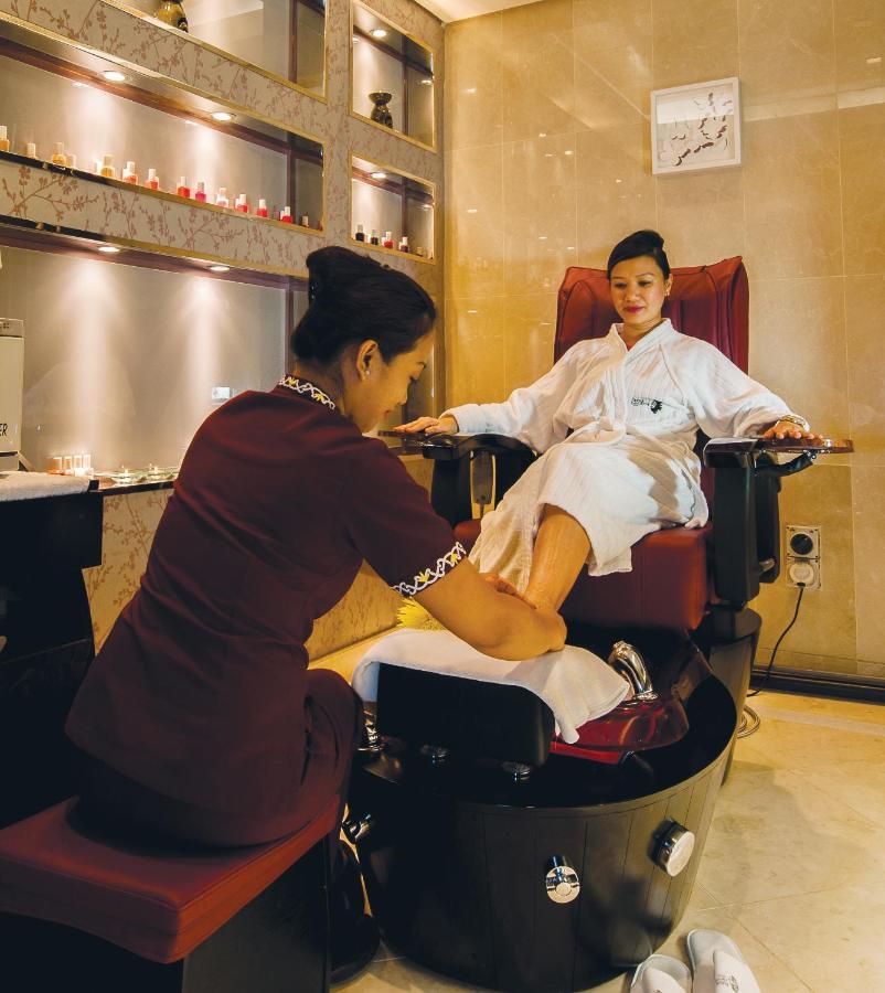 Dubai International Terminal Hotel Exterior foto The photo depicts a spa or wellness setting where a woman is receiving a foot massage or pedicure. She is seated comfortably in a plush chair, wearing a white robe. A technician, dressed in a maroon uniform, is attending to her feet, likely performin