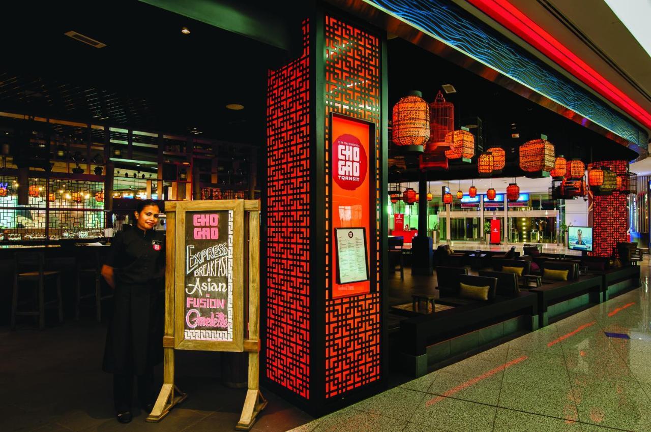 Dubai International Terminal Hotel Exterior foto The photo shows the entrance of a restaurant named "Gho Gho," featuring a prominent sign with the restaurant's name. A staff member in a black uniform stands beside a wooden sign that displays the restaurant's specialty, which is Asian fusion cuisine